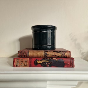 May include: A dark green ceramic planter with white dots sits on top of two vintage books. The top book is red with the title "What Katy Did" and the bottom book is brown with the title "What Katy Did at School".