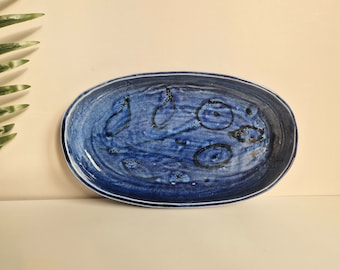 May include: A blue oval ceramic serving dish with a white glaze and abstract black markings.