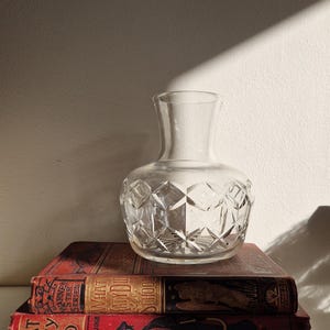 May include: A clear glass vase with a diamond pattern sits on top of two vintage red books. The books are titled "What Katy Did" and "What Katy Did at School".