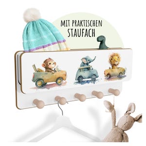 Könnte beinhalten: Ein weißer Wandorganizer aus Holz mit einem Regal und Haken. Der Organizer zeigt eine Aquarellillustration eines Affen, eines Elefanten und eines Löwen in Autos. Eine blau-weiß gestrickte Mütze liegt auf dem Regal. Der Text "MIT PRAKTISCHEN STAUFACH" ist sichtbar.