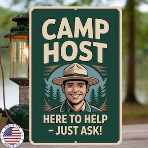 Puede incluir: Un letrero metálico verde oscuro con las palabras "CAMP HOST" en letras color crema. Debajo, una ilustración de un guardabosques sonriente con sombrero. El texto "HERE TO HELP - JUST ASK!" está en la parte inferior.