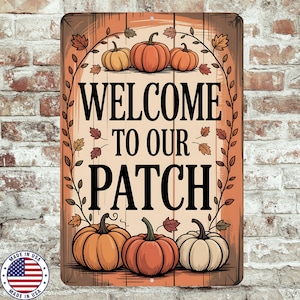 May include: A rectangular metal sign with the text "WELCOME TO OUR PATCH" in black. The sign features illustrations of pumpkins and fall leaves in shades of orange, yellow, and brown. A "MADE IN USA" emblem is in the lower left corner.