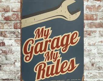 Könnte beinhalten: Rechteckiges Metallschild mit Used-Look. Das Schild zeigt eine große Schraubenschlüssel-Grafik in Creme und Grau auf blauem Hintergrund. Die Worte "My Garage My Rules" sind in einer stilisierten Schrift in Rot und Creme gehalten.
