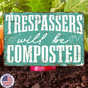 May include: A rectangular, distressed teal metal sign with the words "TRESPASSERS will be COMPOSTED" in white. The sign includes illustrations of a trowel and watering can. The sign is partially buried in soil, with a "Made in USA" emblem in the lower left corner.