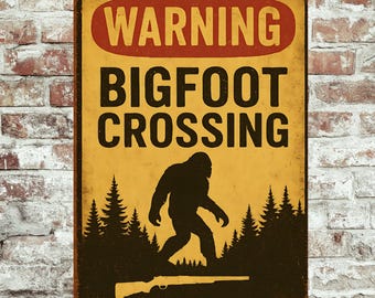 May include: A rectangular metal sign with a distressed finish. The sign features the text "WARNING BIGFOOT CROSSING" in black and red, with a silhouette of Bigfoot and a rifle. The background is yellow.