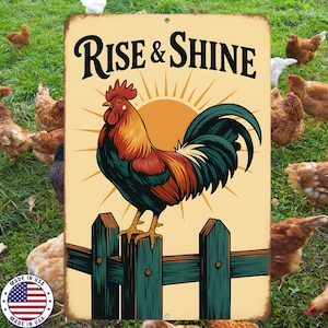 May include: A metal sign with a rooster illustration and the words "Rise & Shine". The rooster is perched on a green fence, with a yellow sun in the background. Chickens are in the background.