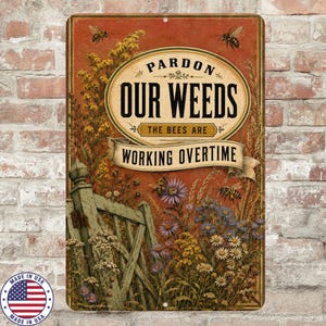 May include: A rectangular metal sign with a rust-colored background featuring a garden scene with a weathered green wooden gate, wildflowers, and bees. The text reads: PARDON OUR WEEDS THE BEES ARE WORKING OVERTIME in black and cream lettering.