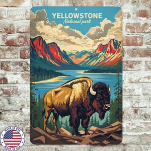 Op de afbeelding: Metalen bord met een illustratie van Yellowstone National Park. Het toont een bizon op de voorgrond, met bergen, een meer en bomen op de achtergrond. Het bord heeft bovenaan de tekst "YELLOWSTONE National park".
