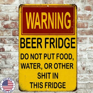 May include: A rectangular metal sign with a yellow background and black text that reads "WARNING BEER FRIDGE DO NOT PUT FOOD, WATER, OR OTHER SHIT IN THIS FRIDGE." The top of the sign is red. A small "Made in USA" emblem is in the lower left corner.