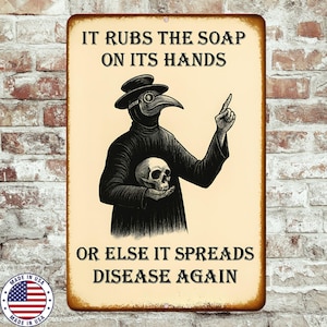 May include: A rectangular metal sign with a distressed finish. The sign features a black and white illustration of a plague doctor holding a skull. Text at the top reads "IT RUBS THE SOAP ON ITS HANDS" and at the bottom "OR ELSE IT SPREADS DISEASE AGAIN."