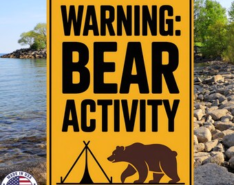 May include: Yellow metal sign with black text reading "WARNING: BEAR ACTIVITY." A brown bear illustration and a tent graphic are below the text. The sign has a white border and a "MADE IN USA" emblem.