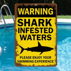 May include: A rectangular metal sign with a yellow background and black text that reads "WARNING SHARK INFESTED WATERS." A black shark silhouette is below the text. The sign also says "PLEASE ENJOY YOUR SWIMMING EXPERIENCE."