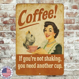 May include: Vintage-style metal sign with the word "Coffee!" in brown script. It features a retro illustration of a woman pouring coffee into a pink cup. The text "If you're not shaking, you need another cup" is below. Includes a "Made in USA" emblem.