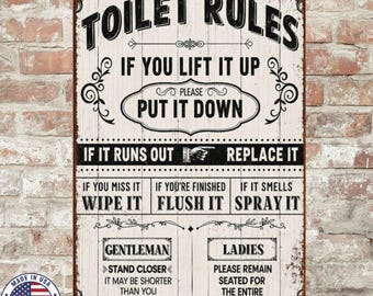 Może przedstawiać: Metalowy szyld w stylu vintage z napisem "TOILET RULES" w kolorze czarnym. Szyld zawiera instrukcje takie jak "PUT IT DOWN" i "REPLACE IT". Posiada również emblemat "MADE IN USA" i humorystyczne porady.