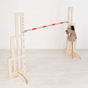 Op de afbeelding: Houten verstelbare hoogte sprong obstakel met een rood-witte paal en een bruin pluche paardenhoofd op een stok. Het obstakel is gemarkeerd met een schaal in centimeters.