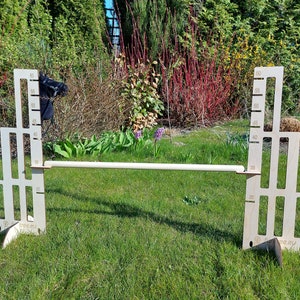 Puede incluir: Un obst&aacute;culo de salto de madera de altura ajustable con una cabeza de caballo negra en el lado izquierdo y una regla a cada lado. El obst&aacute;culo est&aacute; instalado en un c&eacute;sped verde.