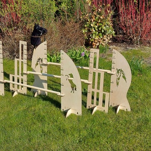 Puede incluir: Tres obst&aacute;culos de salto para caballos de madera con alturas ajustables. Cada obst&aacute;culo presenta una silueta de cabeza de caballo y una regla para medir la altura. Los obst&aacute;culos est&aacute;n instalados en una superficie cubierta de hierba.