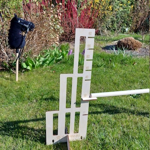 Puede incluir: Un obst&aacute;culo de salto de madera para caballos, con una altura ajustable de 50 a 150 cm. El obst&aacute;culo est&aacute; hecho de madera contrachapada y tiene un acabado blanco. El obst&aacute;culo se muestra en un campo de hierba con un juguete de cabeza de caballo negro en el fondo.