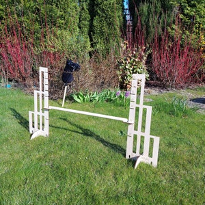 Puede incluir: Un obst&aacute;culo de salto de madera para caballos, con dos paneles verticales con m&uacute;ltiples recortes. El obst&aacute;culo est&aacute; instalado en un campo de hierba.