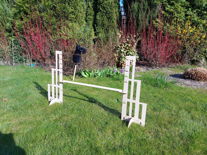 Puede incluir: Un obst&aacute;culo de salto de madera para caballos, con dos paneles verticales con m&uacute;ltiples recortes. El obst&aacute;culo est&aacute; instalado en un campo de hierba.