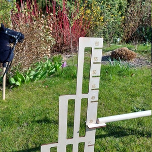 Puede incluir: Un gr&aacute;fico de altura de madera con fondo blanco y n&uacute;meros negros. El gr&aacute;fico est&aacute; marcado en incrementos de 5 cent&iacute;metros, de 20 a 60 cent&iacute;metros. El gr&aacute;fico est&aacute; de pie sobre una superficie de hierba verde.