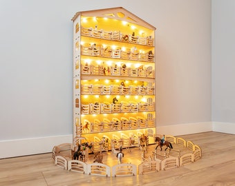 Op de afbeelding: Een houten meerlaags paardenstal met verlichting en miniatuurpaarden erin. De stal heeft een omheind gebied aan de voorkant met miniatuurpaarden en ruiters.