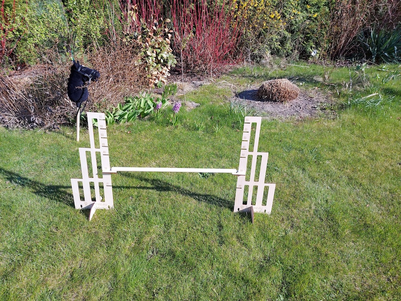 Puede incluir: Un recorrido de obst&aacute;culos de madera para un caballo de juguete, que consta de dos vallas de madera blancas conectadas por una tabla de madera. El recorrido est&aacute; instalado en un c&eacute;sped.