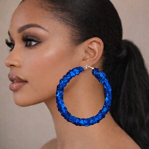 May include: Large, vibrant blue sequin hoop earrings. The earrings are a bright, eye-catching accessory, perfect for adding a touch of glamour. The hoops are round and feature a silver clasp.