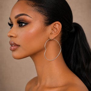 May include: A thin, silver-toned metal hoop earring shaped like a heart. The earring features a smooth, minimalist wire construction that forms a continuous heart outline, secured through the earlobe with a standard post and hinge closure mechanism.