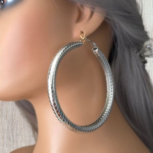 Peut inclure: Boucles d'oreilles créoles argentées avec une finition texturée. Les boucles d'oreilles sont grandes et circulaires.