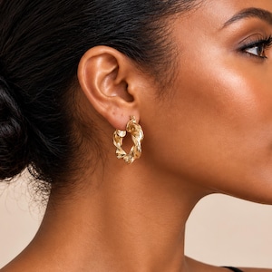 May include: A gold hoop earring with a twisted, textured surface design. The earring features a circular shape with a polished metallic finish that catches the light, creating a series of ridges and valleys along the entire circumference of the hoop.