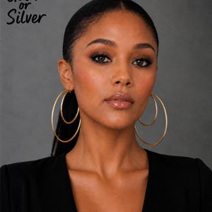May include: A pair of gold-toned double hoop earrings featuring two concentric circular bands of varying sizes. The text "Gold or Silver" is printed in the upper left corner. The earrings have a smooth, polished finish and a thin, lightweight wire construction.