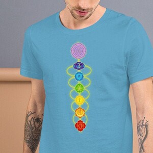 May include: A light blue t-shirt with a colorful chakra symbol design. The symbol is a vertical line of seven overlapping circles, each a different color of the rainbow, with a yellow line connecting them.