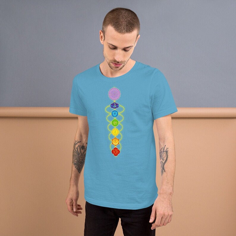 May include: A light blue t-shirt with a colorful chakra symbol design. The symbol is a vertical line of seven overlapping circles, each a different color of the rainbow, with a yellow line connecting them.
