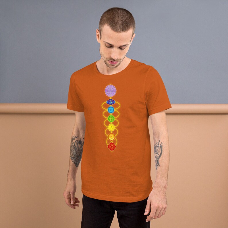 May include: A man is wearing an orange t-shirt with a colorful chakra symbol design. The symbol is a vertical line with seven circles, each a different color, representing the seven chakras.