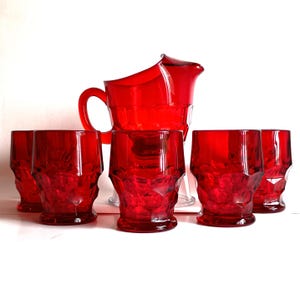 Puede incluir: Un juego de cristalería roja vintage, que incluye una jarra y cinco vasos a juego. La jarra tiene un asa curva y un pico acampanado. Los vasos tienen un diseño facetado. La cristalería está hecha de vidrio rojo transparente.