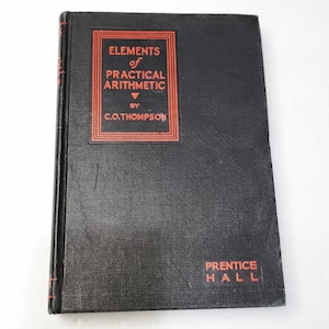 Puede incluir: Un libro negro de tapa dura con el título "Elements of Practical Arithmetic" de C.O. Thompson. El libro está publicado por Prentice Hall.