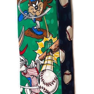May include: A novelty necktie featuring a baseball theme with cartoon characters. The tie has a green background with baseball imagery and cartoon characters. The other side of the tie is navy blue with baseballs.