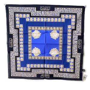 May include: A square scarf with a blue and gold seashell design. The scarf has a dark blue border with the text "Atlantis Paradise Island". The center is a vibrant blue with four seashell illustrations.