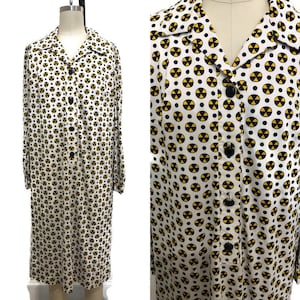 May include: A white long-sleeved dress with a button-up front and a pattern of yellow and black radiation symbols.