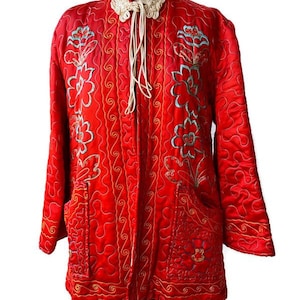 May include: A vibrant red quilted jacket with intricate floral embroidery in turquoise and gold. The jacket features a mandarin collar, long sleeves, and a tie closure. The design includes pockets and a detailed quilted pattern, creating a unique and elegant look.