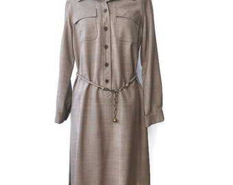 May include: A brown and beige plaid shirt dress with a collared neckline, long sleeves, and a button-up front. The dress has a belt with a gold buckle and a chain detail.