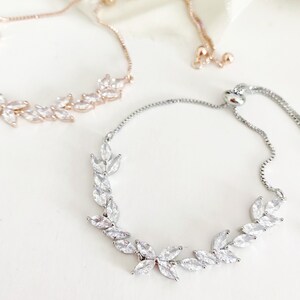 May include: Two delicate bracelets with leaf-shaped crystal accents. One is rose gold, the other silver. Both have adjustable sliding closures. The bracelets are displayed on a white surface.