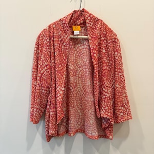 May include: A red and white patterned cardigan hangs on a wooden hanger. The open-front cardigan features a textured design with a mix of red and white dots. The Ruby Rd. brand tag is visible.
