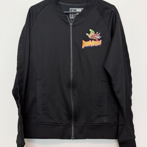 May include: Black zip-up jacket with the Dunkaroos logo on the front. The logo features a cartoon kangaroo with colorful accents. The jacket has a ribbed collar, cuffs, and hem. A New Era logo is visible on the jacket.