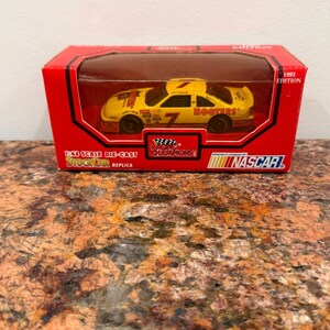 May include: A yellow 1:43 scale die-cast stock car replica in a red box. The car features the number 7 and Hooters branding. The packaging includes the text 1993 Edition, Racing Champions, and NASCAR. The box has a clear plastic window display.