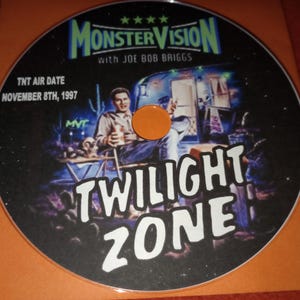 K&ouml;nnte beinhalten: Eine schwarz-wei&szlig;e DVD mit einem Grafikbild eines Mannes in einem Wohnmobil. Der Text "MONSTERVISION with JOE BOB BRIGGS" befindet sich oben auf der DVD. Der Text "TNT AIR DATE NOVEMBER 8TH, 1997" befindet sich oben links auf der DVD. Der Text "TWILIGHT ZONE" befindet sich unten auf der DVD.