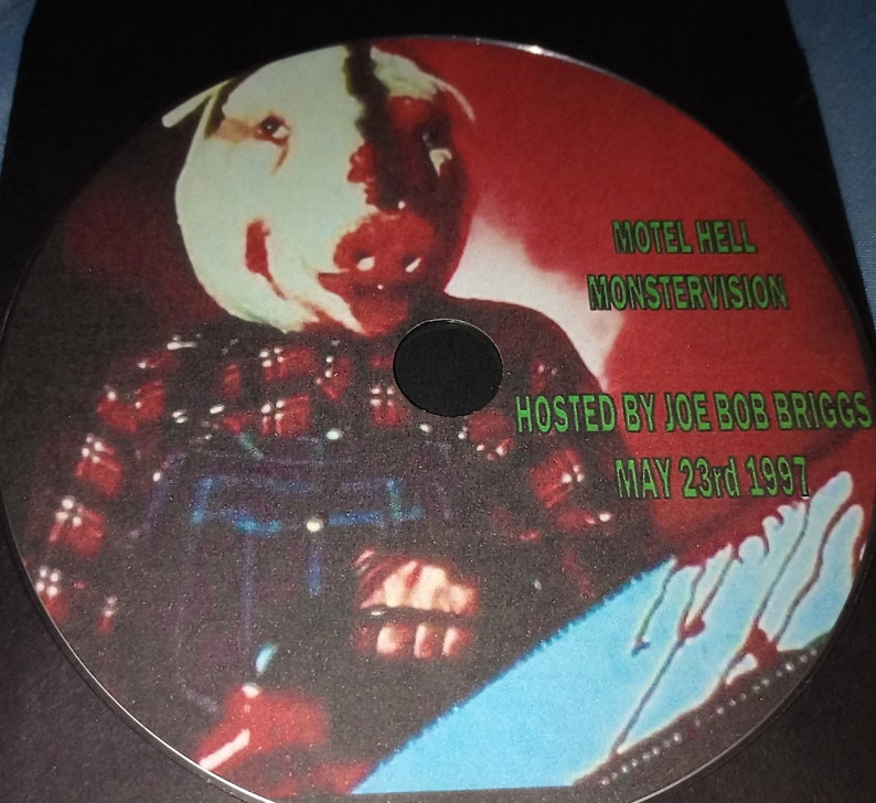 K&ouml;nnte beinhalten: Ein rot-wei&szlig; kariertes Hemd mit einer Kettens&auml;ge und einer Maske. Der Text "Motel Hell MonsterVision Hosted by Joe Bob Briggs May 23rd 1997" befindet sich auf der Scheibe.