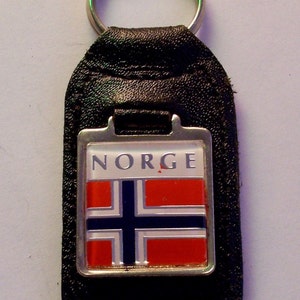 May include: A black leather keychain with a silver metal charm featuring the Norwegian flag and the word "NORGE" in white letters.