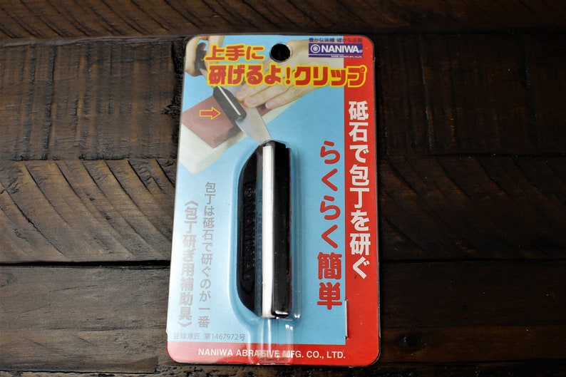 May include: A close-up of a black and white sharpening steel with a blue and red packaging. The packaging has Japanese text that reads "NANIWA" and "らくらく簡単 砥石で包丁を研ぐ" which translates to "Easy and simple, sharpen your knives with a whetstone".